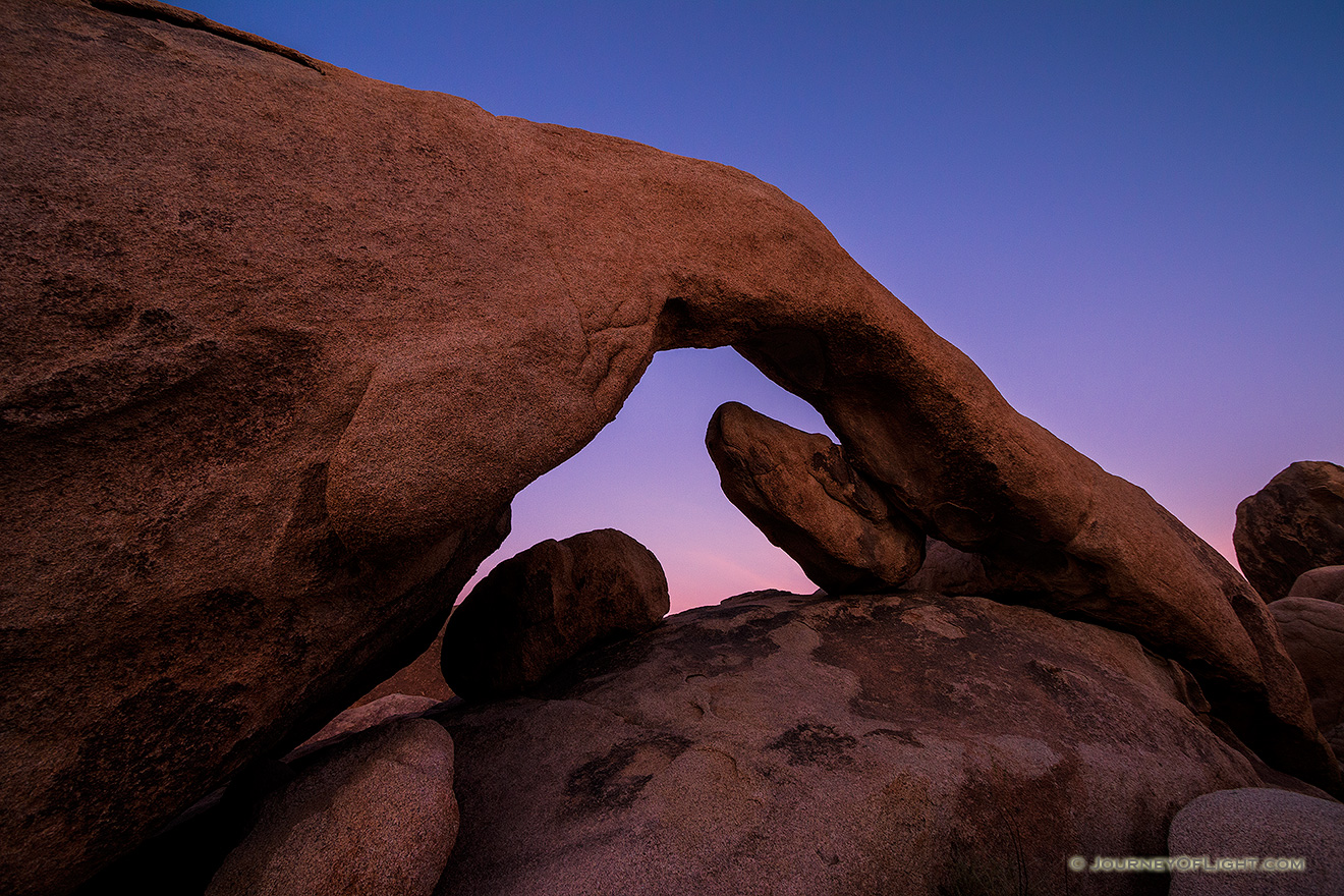 The sky takes on a deep purple hue over the natural arch in Joshua Tree National Park. - State of California Picture