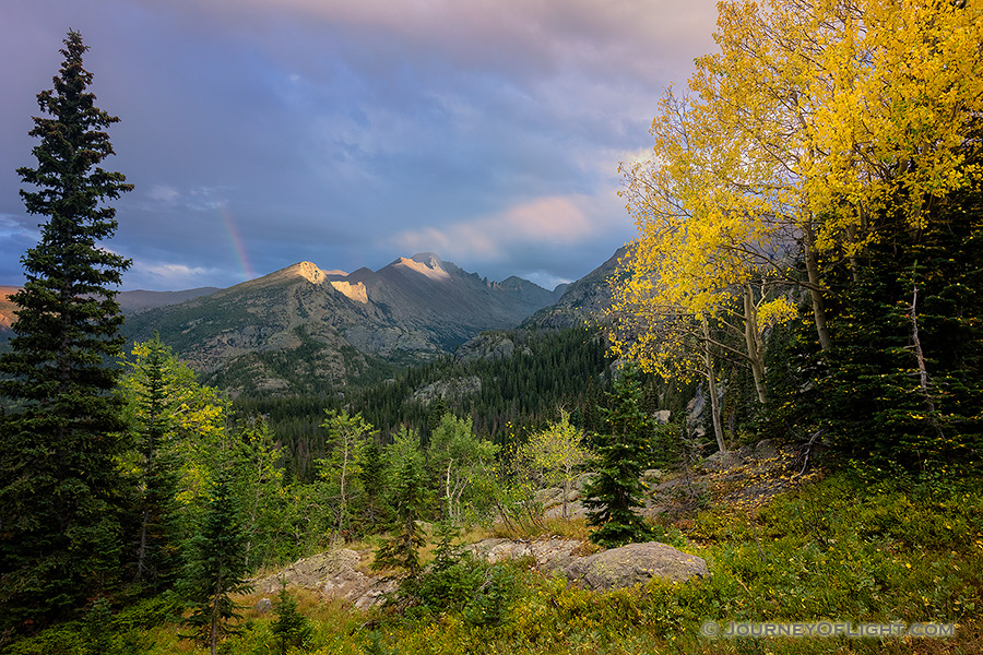 On a cool autumn evening sun strikes the peak of Long's Peak in Rocky Mountain National Park.  A faint rainbow briefly appeared as the storm moved over the mountain. - Colorado Photography
