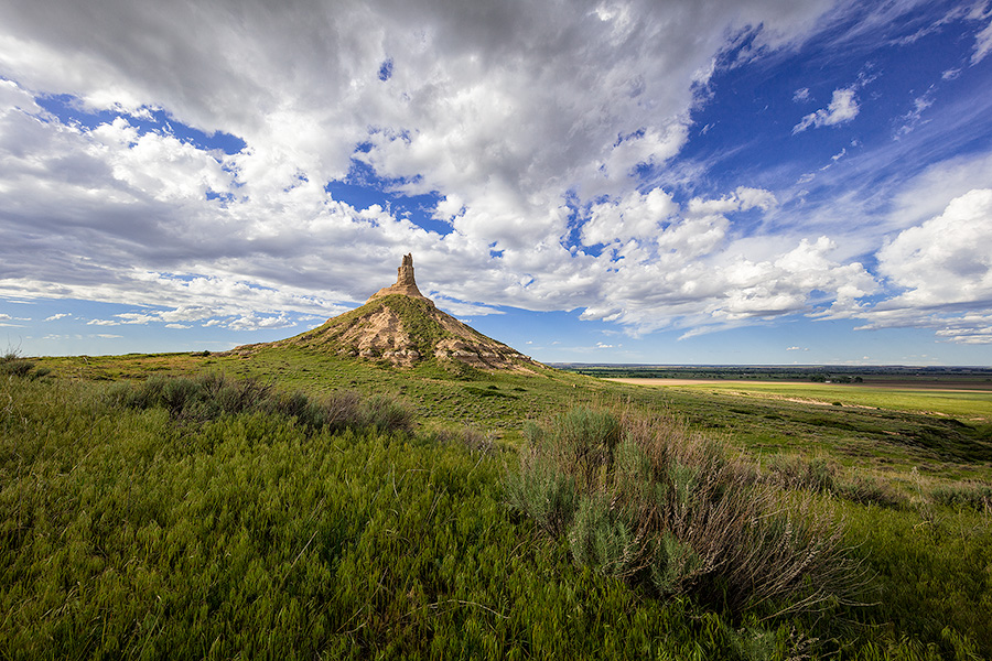 On a cool spring day, under a beautiful blue sky filled with puffy white clouds, Chimney Rock glows in the warm light of the afternoon sun. - Nebraska Photography