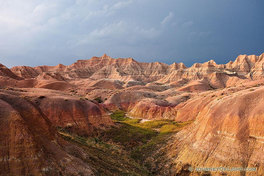 One of the things that I can say about visiting <a href='http://www.journeyoflight.com/journey12/photo-keyword-sort.asp?keywordselected=Badlands National Park'>Badlands National Park</a> in <a href='http://www.journeyoflight.com/journey12/photo-keyword-sort.asp?keywordselected=South Dakota'>South Dakota</a> is that the weather is almost always very dynamic when I am there.  I rarely have times when it is all sunny or all cloudy.  Usually, when the sun bursts forth there is some great color in the sky.  During the day clouds lazily float by and then in the afternoon I am often treated to a spectacular storm.  This image is from one such evening, a summer storm was rolling through and the sunlight was streaming through the clouds illuminating the badlands landscape. - South Dakota Photography