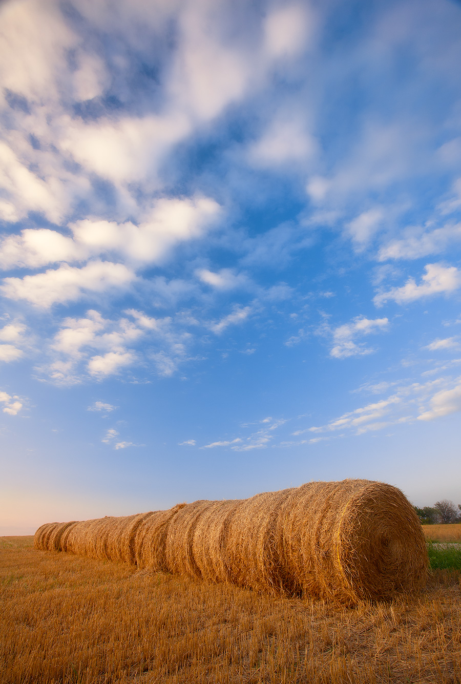 Puffy clouds form in the late evening above a row of hay bales in eastern Nebraska. - Nebraska Photography
