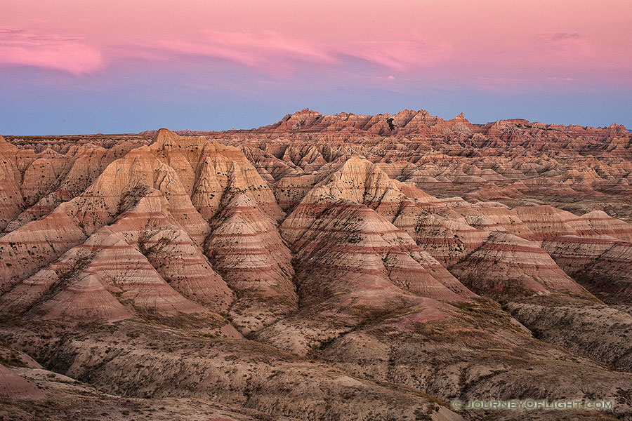 Pink clouds float above Badlands National Park while the rocky terrain below is bathed in the warm light just after sunset. - South Dakota Photography