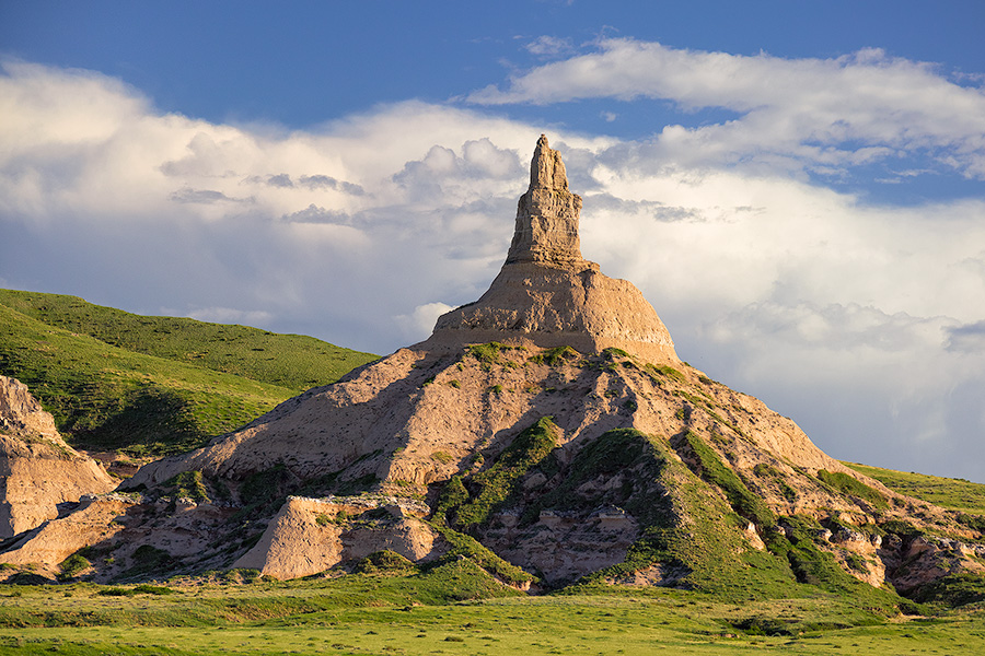 Clouds gather behind Chimney Rock as the glow of the late afternoon sun illuminates its western side. - Nebraska Photography