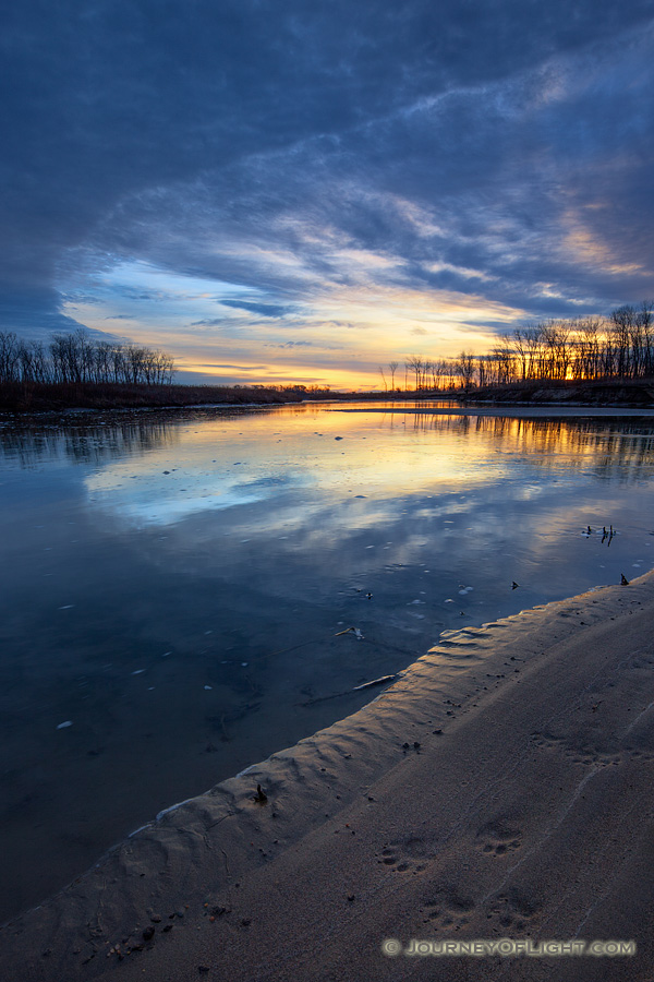 Paw prints from a raccoon are illuminated on the shore as the sun rises over the Missouri River at Ponca State Park in northeastern Nebraska. - Ponca SP Photography