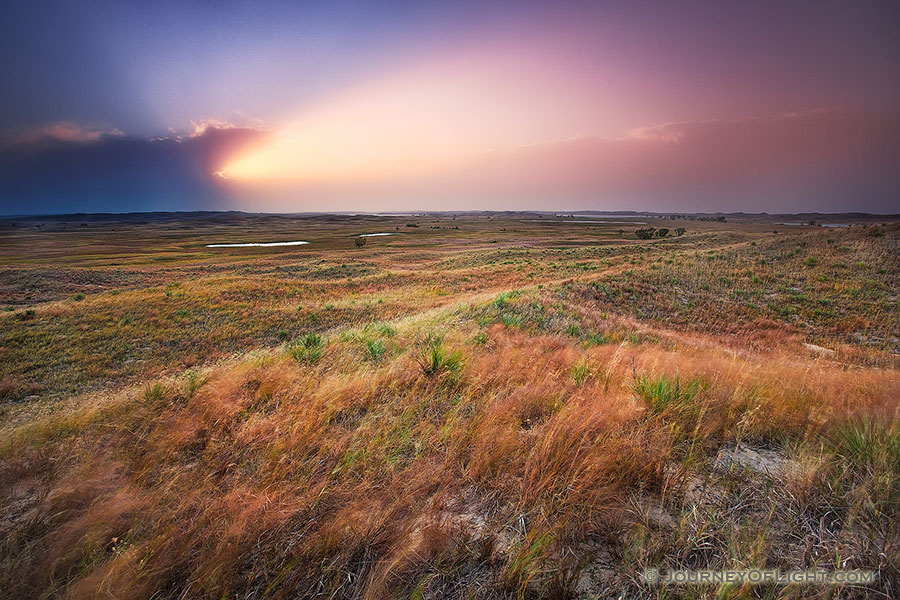 The intense light of the setting sun streams out of clouds in the distance across the sandhills at Valentine National Wildlife Refuge, Nebraska. - Valentine Photography
