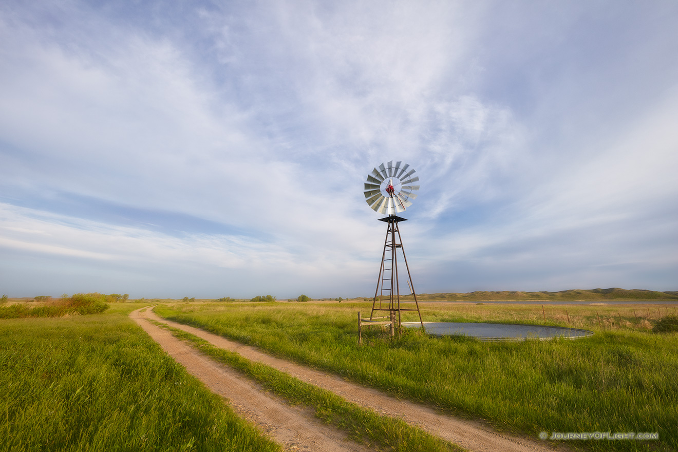 In an area of the Sandhills of Nebraska, far from civilization a two-track road meanders by a windmill and a lake nestled in the hills. - Nebraska Picture