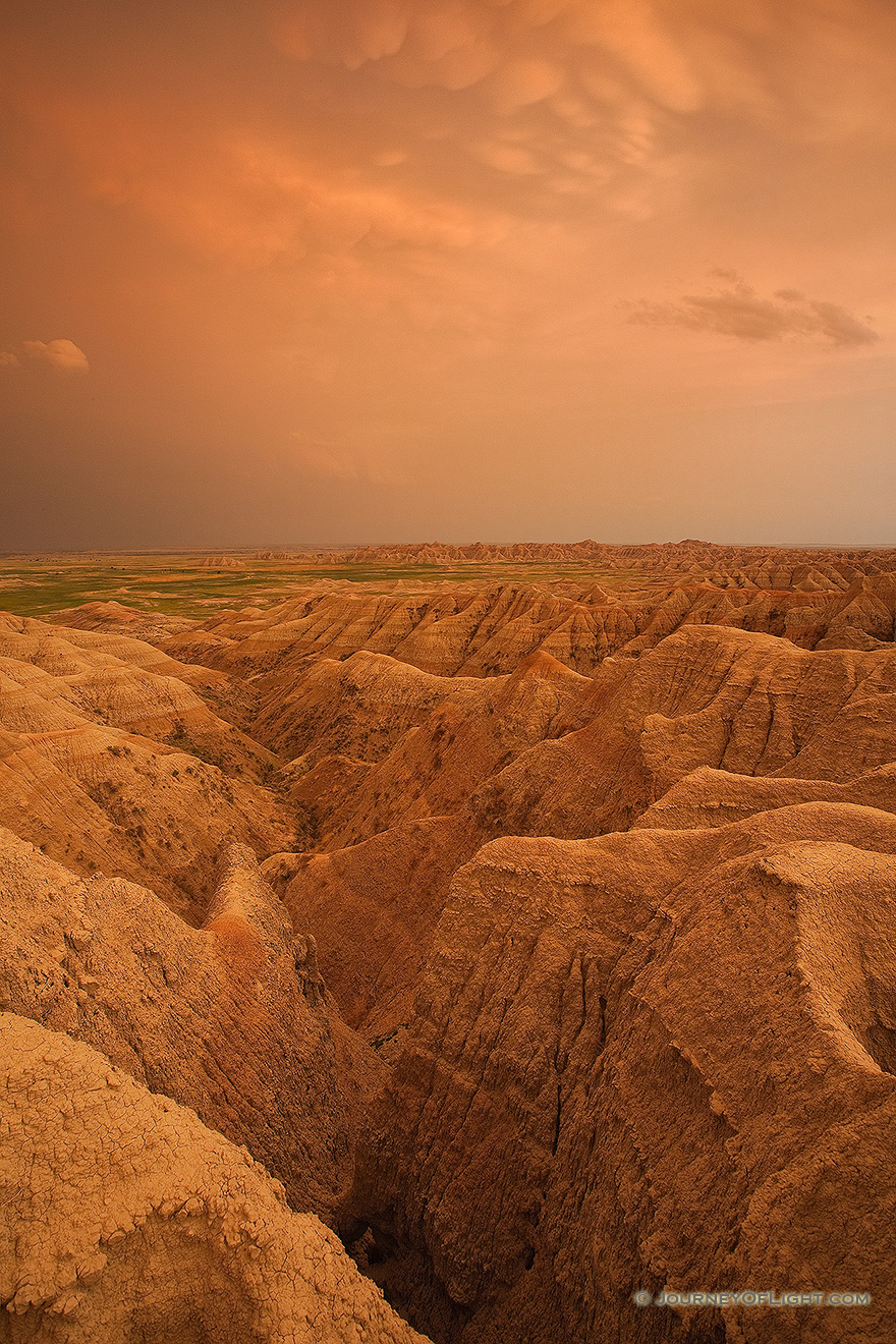 Orange hues from the last light of the setting sun illuminate storm clouds as they pass over Badlands National Park in South Dakota, dark clouds contrast with the desolate landscape. - South Dakota Picture