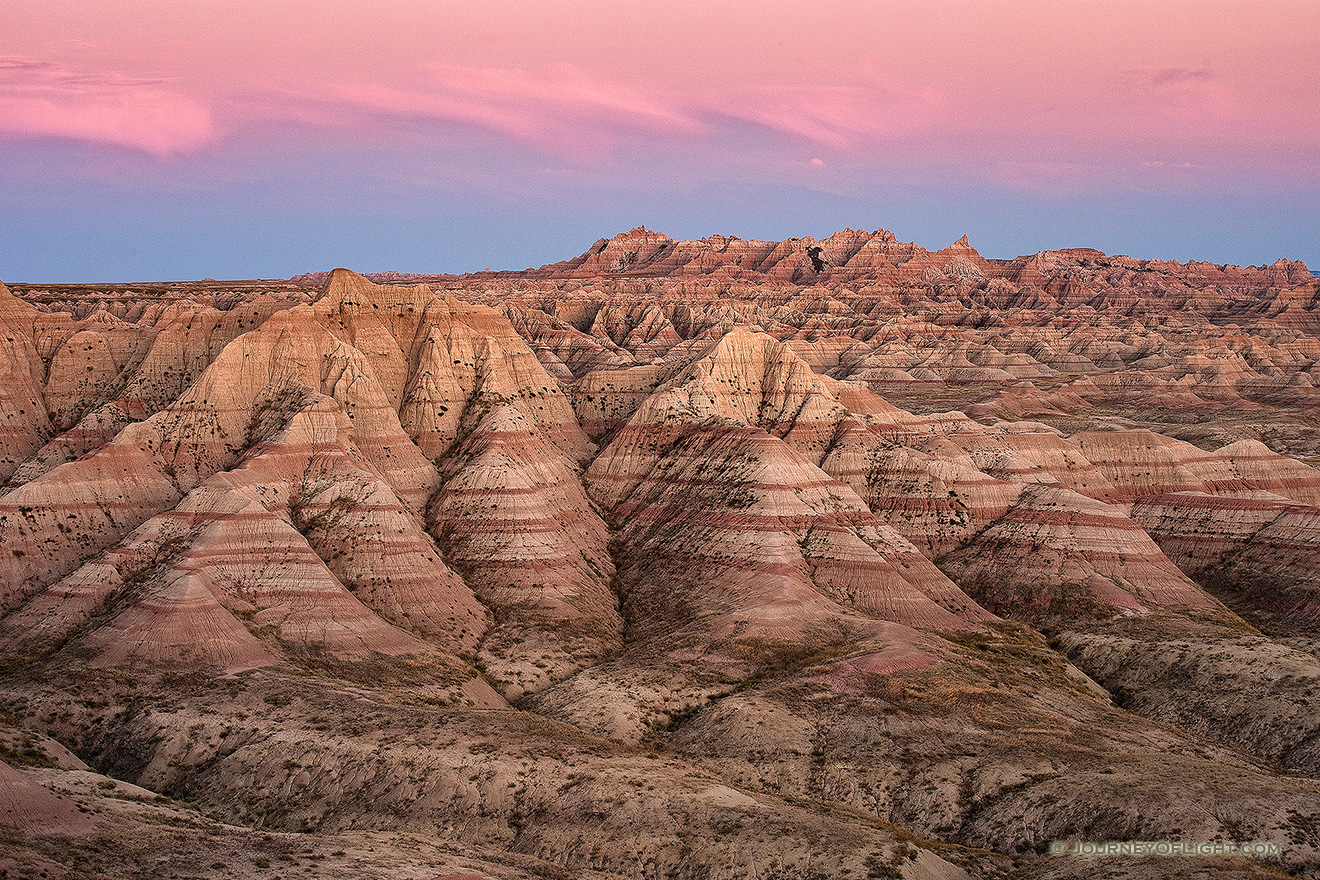 Pink clouds float above Badlands National Park while the rocky terrain below is bathed in the warm light just after sunset. - South Dakota Picture