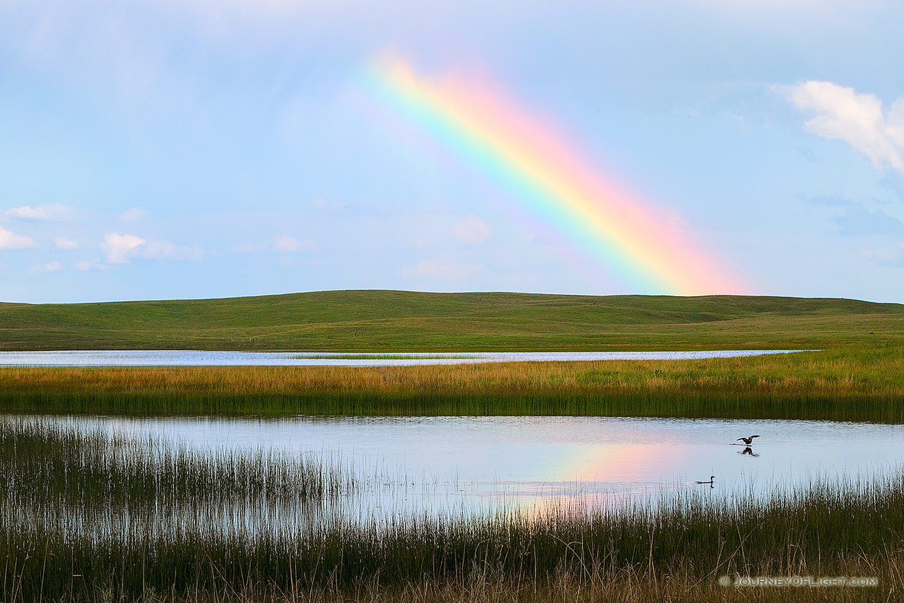 A rainbow appears reflected in a small lake after a storm in the Sandhills of Nebraska. - Nebraska Picture