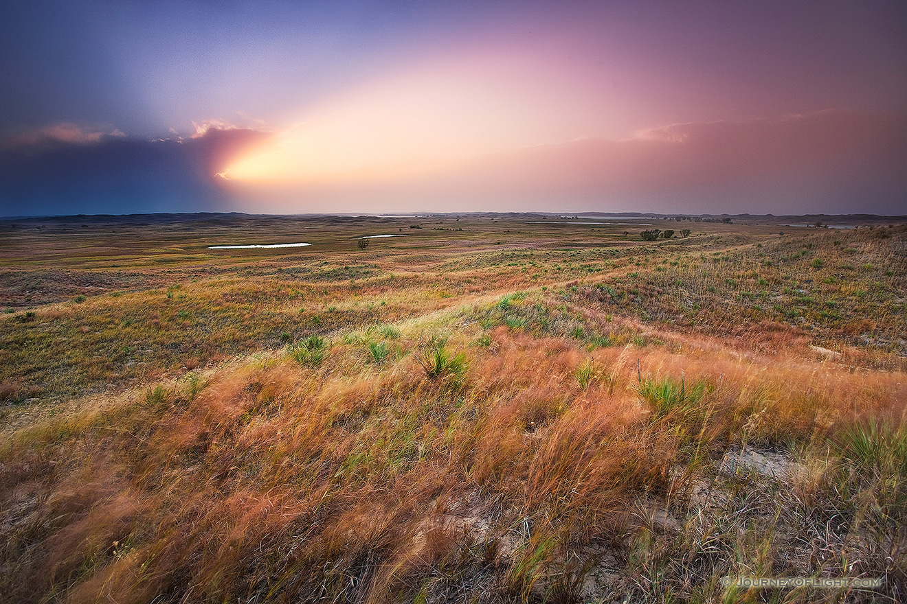 The intense light of the setting sun streams out of clouds in the distance across the sandhills at Valentine National Wildlife Refuge, Nebraska. - Valentine Picture