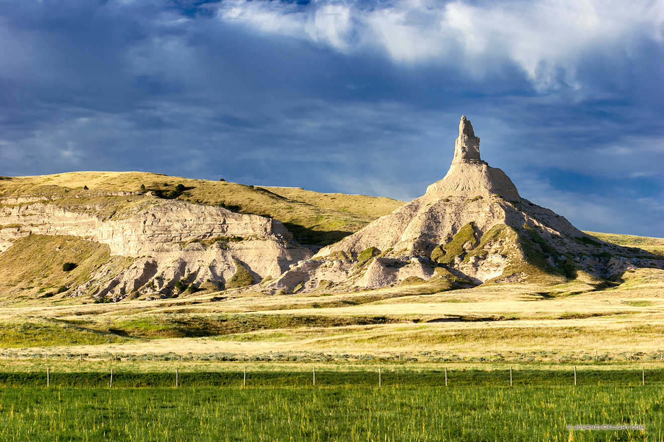 The spire known as Chimney Rock glows warm in the recent sunrise and the surrounding fields are a verdant green from a recent rain. - Nebraska Picture