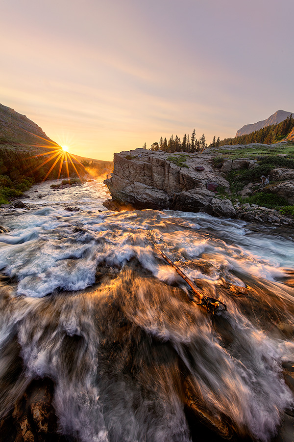 A scenic landscape photograph of sunrise over a waterfall Swiftcurrent Lake, Glacier National Park, Montana. - Glacier Photography