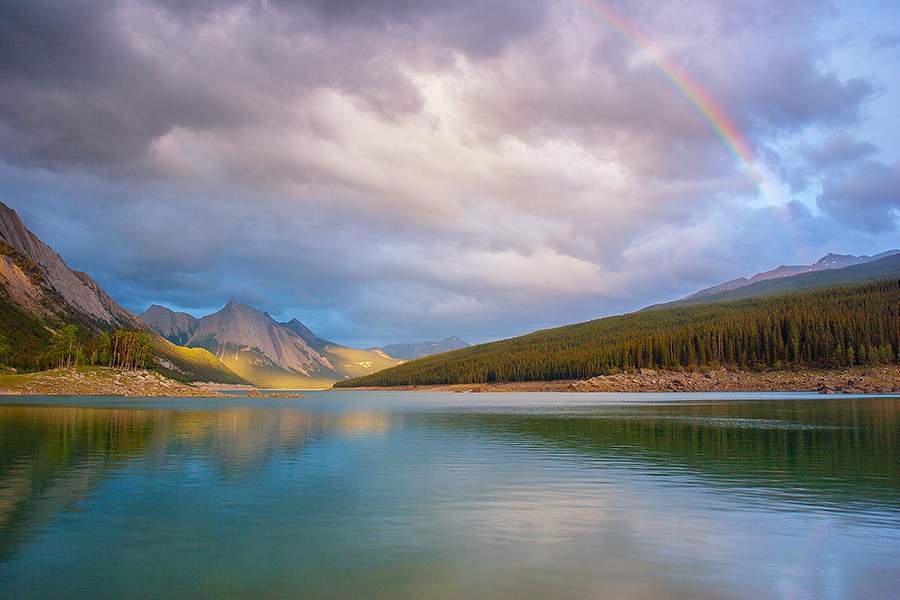 A Rainbow is visible above Medicine Lake in Jasper National Park, Alberta, Canada.  This photograph was captured just as the last rays of the sun peeked through the clouds around 10:30 pm. - Jasper Photography